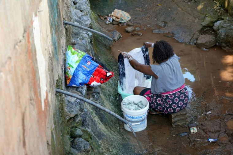 Une femme lave des vêtements à une fontaine publique distribuant de l'eau non potable à Cavani, un bidonville de Mamoudzou, le 31 octobre 2025 à Mayotte  ( AFP / Marine GACHET )