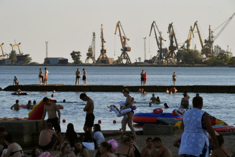 Des estivants profitent de la plage à Marioupol, citée ukrainienne contrôlée par la Russie, avec le port de commerce à l'arrière-plan, le 14 juillet 2025 ( AFP / Olga MALTSEVA )