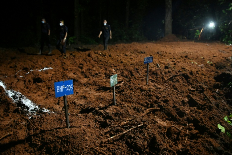 Des agents de police marchent à proximité de tombes de victimes non identifiées de la crue dévastatrice, le 30 août 2026 à Devghat au Népal ( AFP / Prakash MATHEMA )