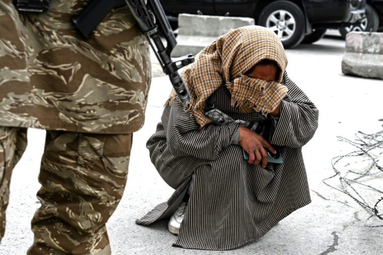 Un officier de sécurité taliban monte la garde à côté de Samira Muhammadi pleurant son fils de 20 ans, Aref Khan, tué par une frappe aérienne pakistanaise sur un hôpital pour toxicomanes, lors des funérailles collectives de victimes à la mosquée Eid Gah de Kaboul le 26 mars 2026 en Afghanistan ( AFP / Wakil Kohsar )