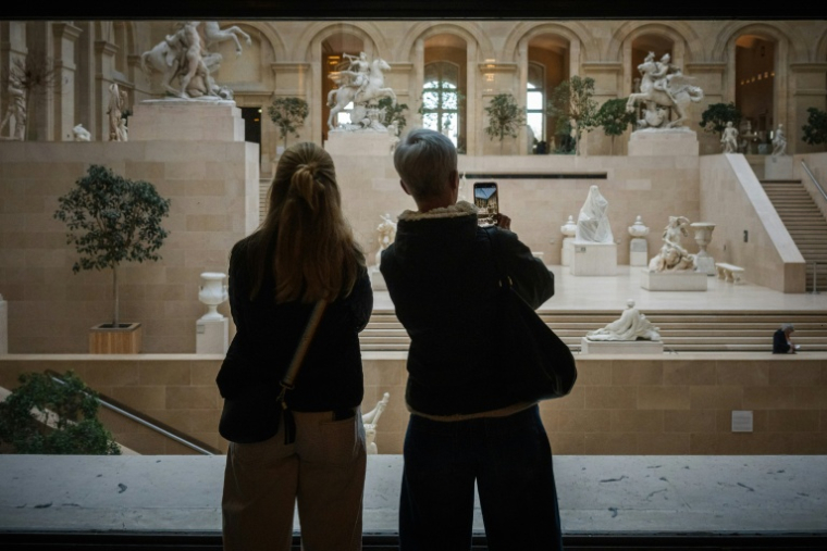 Des touristes observent l'intérieur du musée du Louvre, fermé lors d'une grève du personnel, le 15 décembre 2025 à Paris ( AFP / Dimitar DILKOFF )