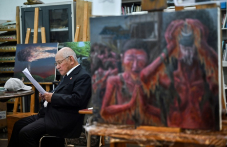 Masaki Hironaka, un survivant de la bombe atomique, assis parmi des peintures réalisées par des élèves pour préserver les témoignages des survivants, le 29 mai 2025 à Hiroshima  ( AFP / Richard A. Brooks )