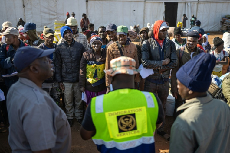 Des migrants attendent d'être appelés pour monter à bord d'un bus à destination du Zimbabwe, depuis le camp de transit de Musina en Afrique du Sud, le 9 juillet 2026 ( AFP / EMMANUEL CROSET )