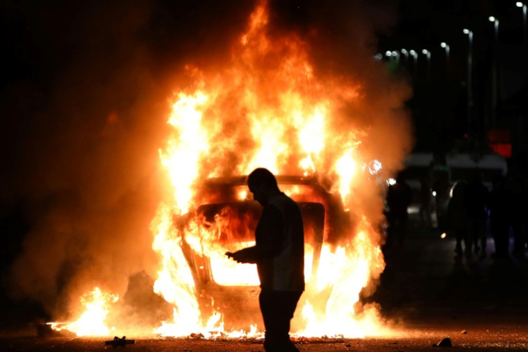 Une voiture en feu lors d'émeutes visant des immigrés à Ballymena, le 10 juin 2025 en Irlande du Nord ( AFP / PAUL FAITH )