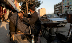 Un barbier coupe les cheveux d'un client dans une rue de Kaboul le 11 février 2026 ( AFP / Wakil KOHSAR )