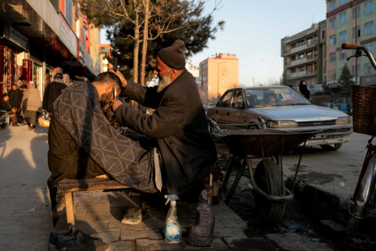 Un barbier coupe les cheveux d'un client dans une rue de Kaboul le 11 février 2026 ( AFP / Wakil KOHSAR )