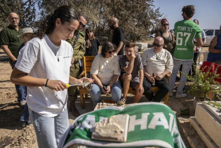 Des habitants du kibboutz de Kfar Aza dans le sud d'Israël, se recueillent devant une tombe lors d'une cérémonie en hommage aux personnes tuées lors de l'attaque du Hamas le 7 octobre 2023, le 16 octobre 2025 ( AFP / Maya Levin )