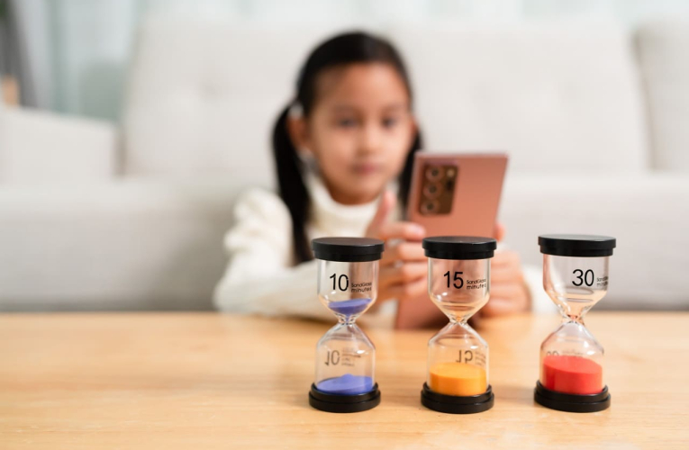 (Crédits photo : Adobe Stock - Petite fille regardant l'écran d'un smartphone, devant des sabliers qui mesurent le temps passé)