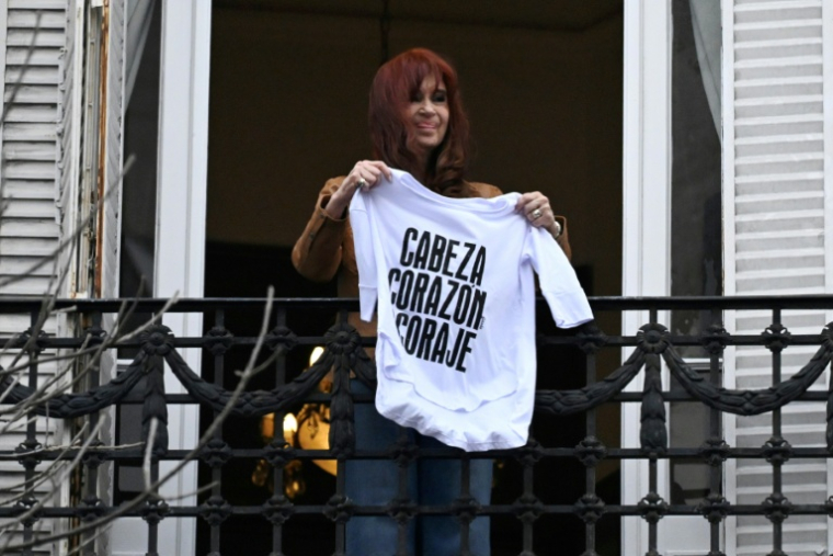 L'ancienne présidente et vice-présidente argentine, Cristina Kirchner, tient un t-shirt "Tête, coeur, courage" alosr qu'elle salue ses partisans depuis le balcon de sa résidence à Buenos Aires, le 20 septembre 2025, au 100e jour de son arrestation ( AFP / Luis ROBAYO )