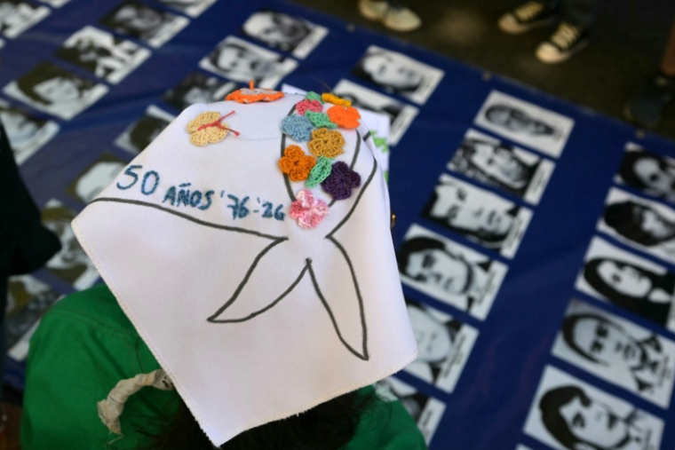 Une femme porte un foulard blanc brodé du symbole des Mères de la Plaza de Mayo devant les portraits de personnes disparues pendant la dictature militaire, lors des commémorations du 50e anniversaire du coup d’État militaire à Buenos Aires, le 24 mars 2026 en Argentine ( AFP / Juan Mabromata )