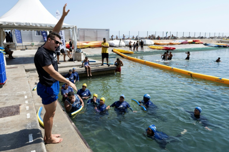 Des mères des quartiers Nord de Marseille écoutent un maître-nageur lors d'un cours de natation dispensé par l'association "Le Grand Bleu" dans une piscine d'eau de mer près du port de l'Estaque, le 11 août 2025 ( AFP / Miguel MEDINA )