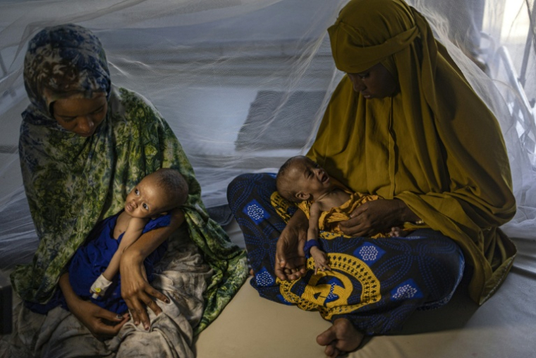 Des femmes somaliennes récemment déplacées tiennent dans leurs bras leurs bébés souffrant de malnutrition sévère dans un centre de santé, à Kismayo, le 22 avril 2026  ( AFP / SIMON MAINA )