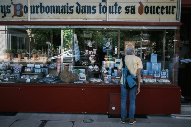 Un client regarde les boîtes de pastilles Vichy et les produits exposés dans la vitrine d'une boutique de la confiserie Maison Moinet à Vichy, le 13 mai 2025 dans l'Allier ( AFP / JEAN-PHILIPPE KSIAZEK )