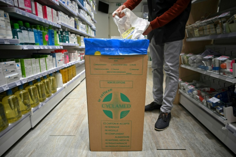Un homme jette des médicaments non utilisés dans une boîte en carton de l'organisme Cyclamed, chargé de leur collecte, le 23 mars 2023 dans une pharmacie à Colomiers ( AFP / Valentine CHAPUIS )