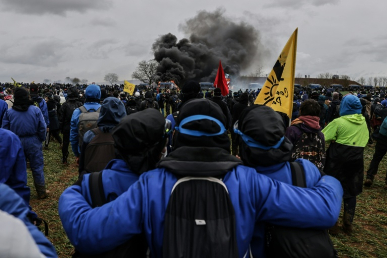 Des manifestants regardent un fourgon de gendarmerie brûler lors de la manifestation contre une "mégabassine" à Sainte-Soline (Deux-Sèvres), le 25 mars 2023 ( AFP / THIBAUD MORITZ )