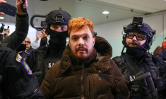 Le trafiquant de drogue français Mohamed Amra, escorté par des policiers à l'aéroport international d'Otopeni, près de Bucarest, en Roumanie, le 25 février 2025, avant d'embarquer à bord d'un avion pour être extradé vers la France ( AFP / Octav Ganea )
