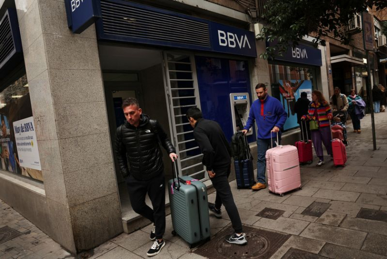 Des personnes portant des valises passent devant une agence de la banque BBVA à Madrid.