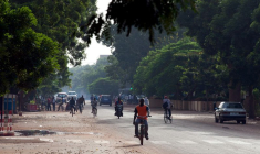 Des personnes se déplacent à vélo et à moto dans une rue de Ouagadougou