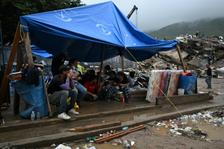 Des rescapés du double séisme s’abritent sous une bâche tandis que les secouristes fouillent les décombres des immeubles effondrés à Caraballeda, dans l’État de La Guaira, au Venezuela, le 11 juillet 2026 ( AFP / Raul ARBOLEDA )