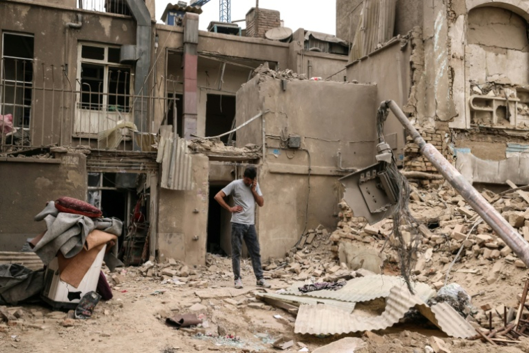 Un homme au téléphone devant des habitations détruites, le 15 mars 2026 à Téhéran  ( AFP / Atta KENARE )