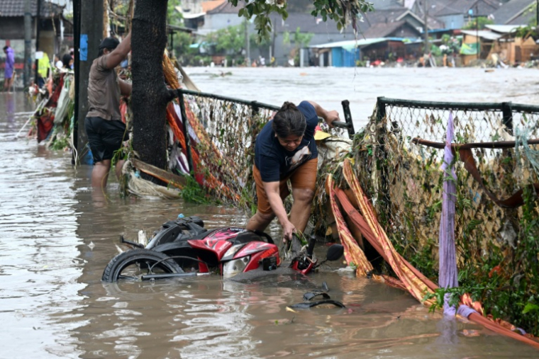 Une habitante touchée par les inondations redresse une moto immergée dans son quartier après de fortes pluie, à Denpasar, sur l’île indonésienne de Bali, le 10 septembre 2025 ( AFP / SONNY TUMBELAKA )