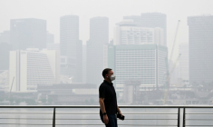 Un passant porte un masque de protection le long du boulevard à Marina Bay, noyé dans la brume, le 12 octobre 2026 à Singapour  ( AFP / Roslan RAHMAN )