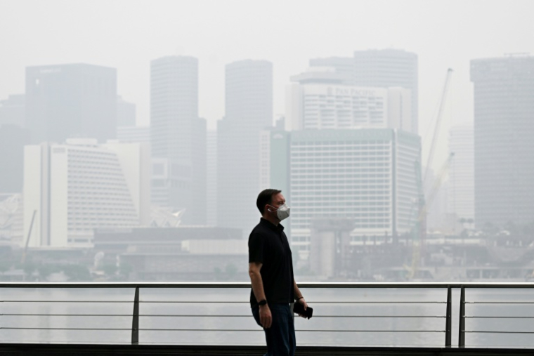 Un passant porte un masque de protection le long du boulevard à Marina Bay, noyé dans la brume, le 12 octobre 2026 à Singapour  ( AFP / Roslan RAHMAN )