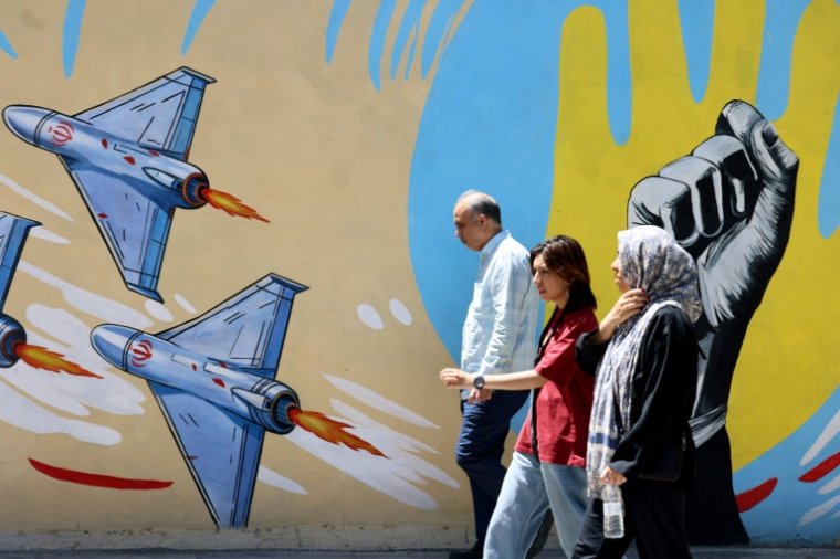Des Iraniens passent devant des graffitis anti-américains et anti-israéliens, à Téhéran le 10 mai 2026 ( AFP / ATTA KENARE )
