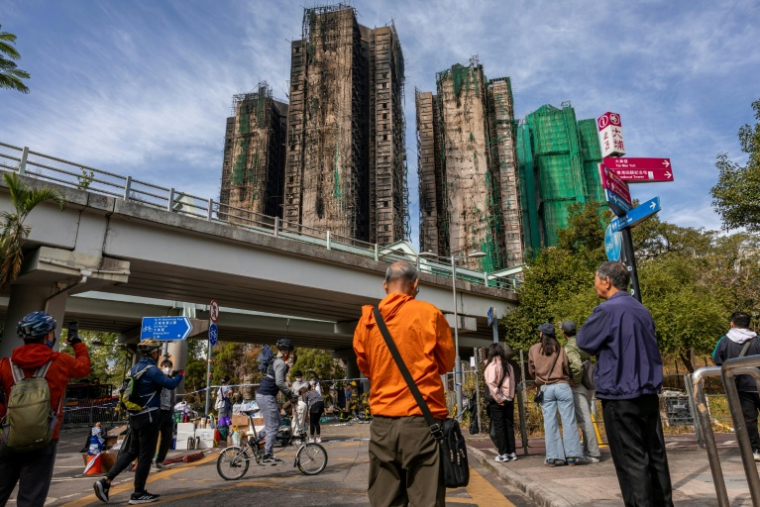 Des passants regardent les tours du coplexe complexe résidentiel Wang Fuk Court ravagées par un incendie, le 28 novembre 2025 à Hong Kong ( AFP / Dale DE LA REY )