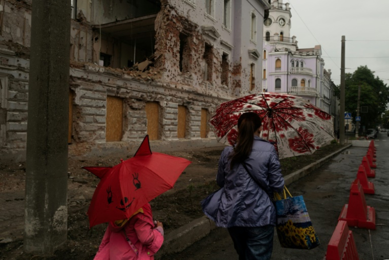 Une mère et sa fille passent près d'un bâtiment détruit par un bombardement russe, le 12 juin 2025 à Soumy, dans le nord-est de l'Ukraine ( AFP / Florent VERGNES )