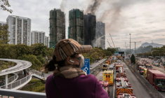 Une femme se tient à distance, jeudi 27 novembre 2025 à Hong Kong, de l'incendie sur les tours résidentielles qui s'est déclaré la veille ( AFP / Dale DE LA REY )