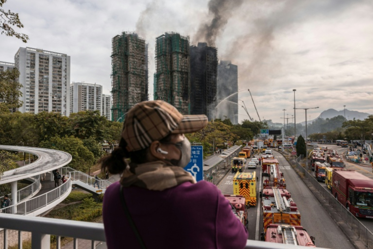 Une femme se tient à distance, jeudi 27 novembre 2025 à Hong Kong, de l'incendie sur les tours résidentielles qui s'est déclaré la veille ( AFP / Dale DE LA REY )