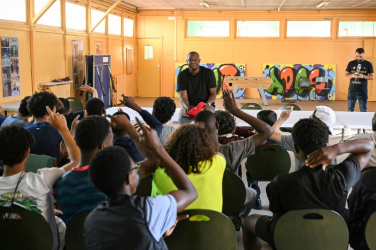 L'ex-détenu Adama Camara s'entretient avec des écoliers après une visite de sa "Grotte Mobile", un camion où il a reconstitué son ancienne cellule pour "sensibiliser" les jeunes à la vie en prison, le 11 juin 2025 à Drancy, en Seine-Saint-Denis ( AFP / Hugo MATHY )