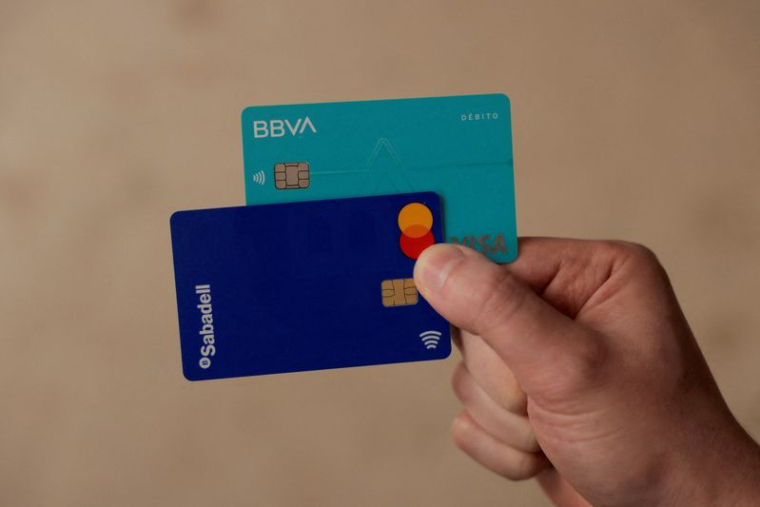 Un homme montre ses cartes de débit des banques BBVA et Sabadell