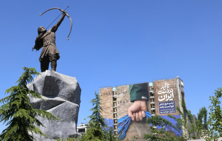 Une sculpture moderne d'Arash l'Archer, figure légendaire de la mythologie persane, devant affiche géante sur la façade d'un immeuble représentant le détroit d'Ormuz avec l'inscription en persan "À jamais dans la main de l'Iran", le 25 mai 2026 à Téhéran ( AFP / ATTA KENARE )