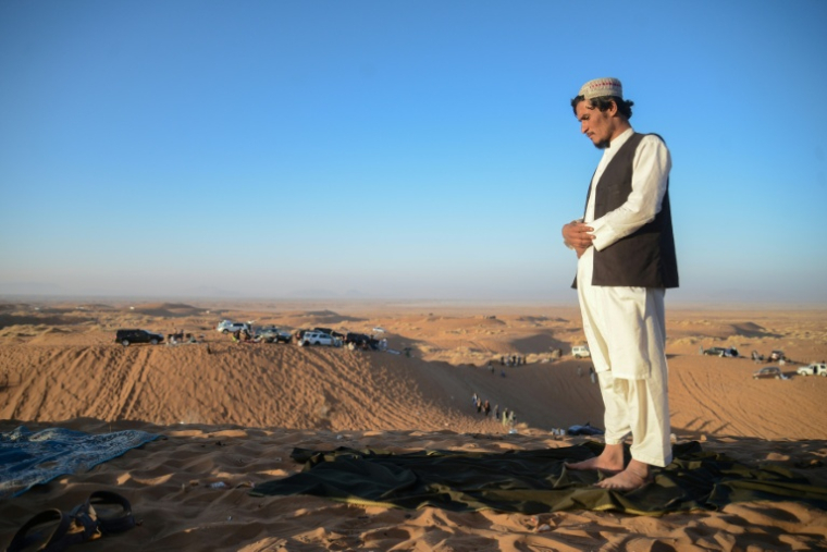 Un homme prie alors que des passionnés d'automobile conduisent des 4X4 dans les dunes de la province de Kandahar, le 5 décembre 2025  en Afghanistan ( AFP / Sanaullah SEIAM )
