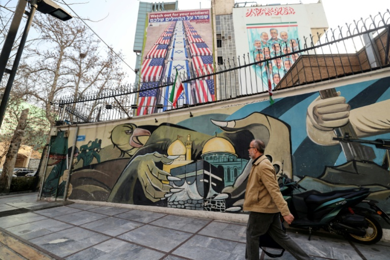 Un Iranien passe devant des fresques murales anti-américaines et anti-israéliennes, le 27 janvier 2026 à Téhéran  ( AFP / ATTA KENARE )