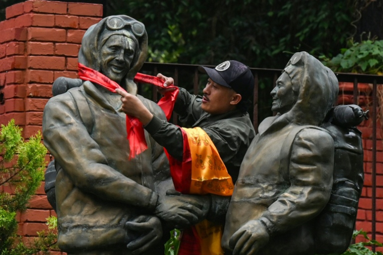 Un alpiniste dépose des écharpes cérémonielles sur les statues de Tenzing Norgay (D) et d'Edmund Hillary (G) pour  le 73e anniversaire de la première ascension du mont Everest à Katmandou, le 29 mai 2026 ( AFP / PRAKASH MATHEMA )