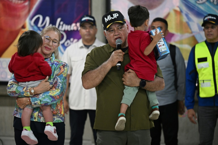 Le ministre vénézuélien de l'Intérieur Diosdado Cabello s'exprime en portant un enfant rapatrié aux côtés de la Première Dame Cilia Flores après l'arrivée d'un avion transportant des migrants vénézuéliens rapatriés des États-Unis à l'aéroport international Simon Bolivar à Maiquetia, au Venezuela, le 18 juillet 2025 ( AFP / Federico PARRA )