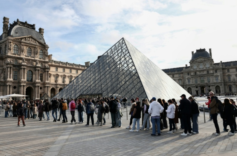 Des visiteurs font la queue devant la Pyramide du Louvre, conçue par l'architecte sino-américain Ieoh Ming Pei, et le musée du Louvre le jour de sa réouverture après un vol de bijoux, le 22 octobre 2025 à Paris ( AFP / Thibaud MORITZ )