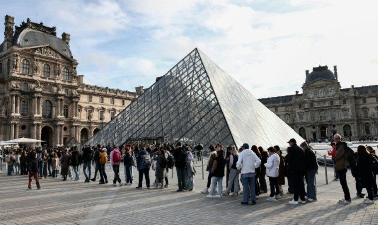 Des visiteurs font la queue devant la Pyramide du Louvre, conçue par l'architecte sino-américain Ieoh Ming Pei, et le musée du Louvre le jour de sa réouverture après un vol de bijoux, le 22 octobre 2025 à Paris ( AFP / Thibaud MORITZ )