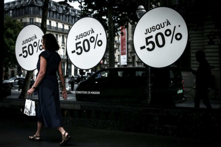Une passante marche à côté d'une vitrine annonçant les soldes, le 25 juin 2025 à Paris ( AFP / Thibaud MORITZ )
