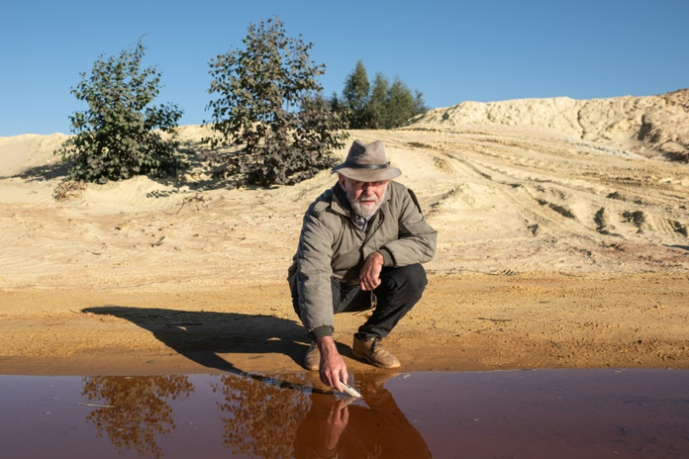 David van Wyk, chercheur principal à la Bench Marks Foundation, effectue des tests dans un cours d'eau à la décharge de la mine de Snake Park, à Soweto, le 30 mai 2025 en Afrique du Sud ( AFP / EMMANUEL CROSET )