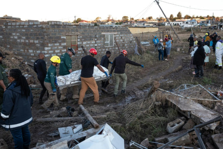Des membres des services médicaux d'urgence (EMS) sortent des corps d'une maison après des inondations hivernales, le 12 juin 2025 près de Mthatha, en Afrique du Sud ( AFP / EMMANUEL CROSET )