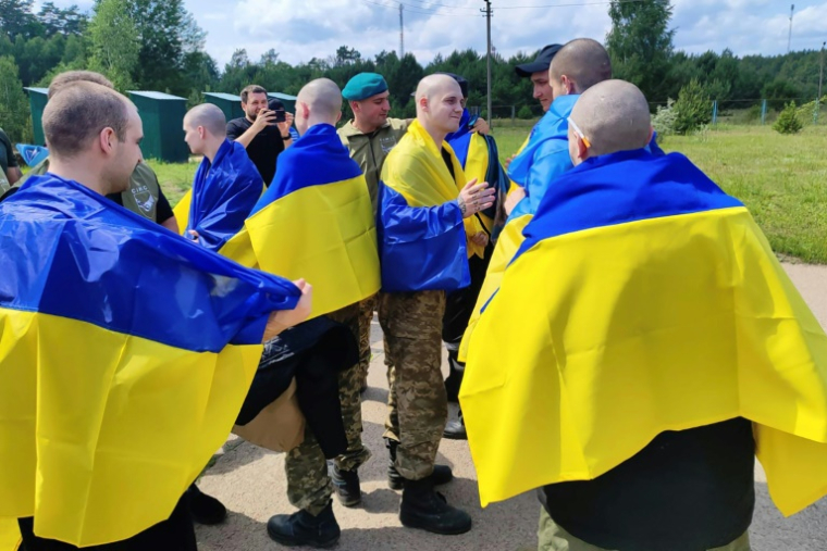 Photo prise et diffusée par le service de presse présidentiel ukrainien, le 9 juin 2025, de prisonniers de guerre ukrainiens enveloppés de drapeaux nationaux après un échange dans un lieu non divulgué ( Service de presse de la présidence ukrainienne / Handout )