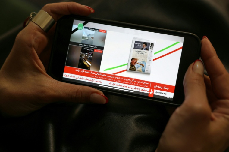 Une Iranienne regarde un journal télévisé sur une chaîne de télévision d'État iranienne sur son téléphone portable à Téhéran, le 25 mars 2026 ( AFP / - )