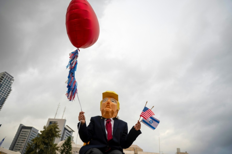 Une personne à Tel-Aviv, portant un masque à l'effigie du président américain Donald Trump, brandit les drapeaux américain et israélien, après l'annonce de l'accord sur Gaza, le 9 octobre 2025 ( AFP / Maya Levin )