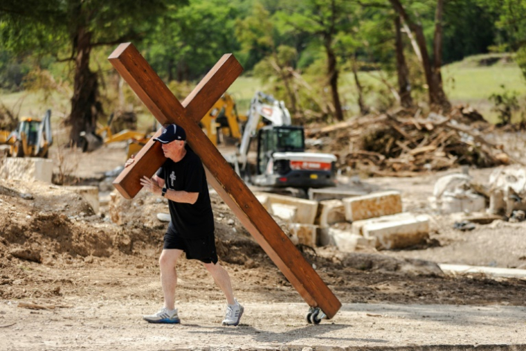 Un homme marche sur les rives du fleuve Guadalupe en emportant une grande croix de bois, à Ingram, Texas, le 8 juillet 2025 ( GETTY IMAGES NORTH AMERICA / Jim Vondruska )