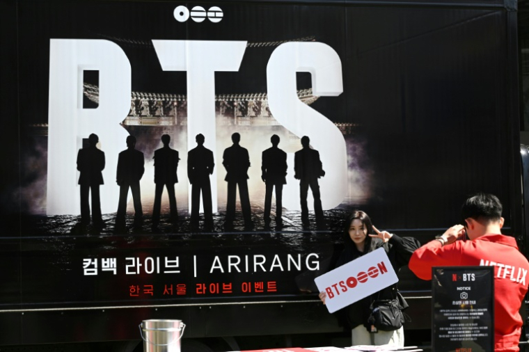 Une femme pose pour une photo devant un camion faisant la promotion du concert de retour du boys band de K-pop BTS à Séoul, le 19 mars 2026 ( AFP / Jung Yeon-je )