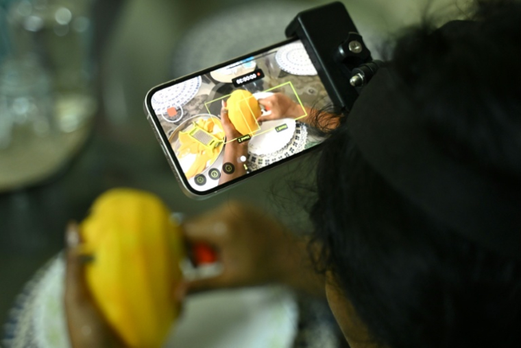 Nagireddy Sriramyachandra filme avec un téléphone ses gestes pendant qu'elle coupe une mangue pour entraîner un futur robot dopé à l'IA, le 15 mai 2026 à Madras, en Inde ( AFP / R.Satish BABU )